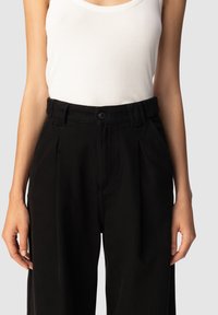 Pantalones de talle alto negros con pliegues, confeccionados con tejido texturizado, que cuentan con un cierre frontal de botón y bolsillos laterales.