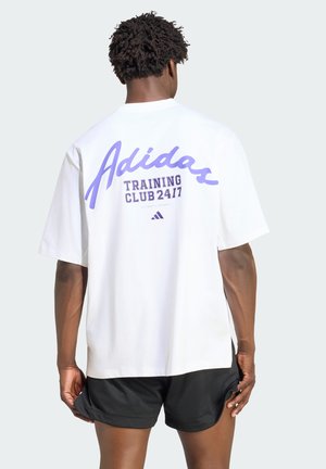 Homme de dos portant un t-shirt blanc Adidas avec le texte « Training Club 24/7 » et un short de sport noir sur un fond uni.