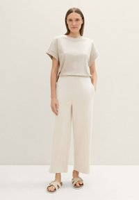 Camisa beige de manga corta con un corte relajado, combinada con pantalones crema de pierna ancha de cintura alta y sandalias beige con detalle de hebilla.