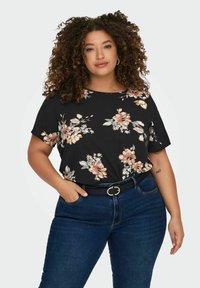 Blusa nera a fiori con maniche corte e scollatura rotonda, caratterizzata da motivi floreali rosa e bianchi. Abbinata a jeans blu scuro e una cintura nera.
