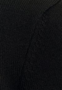 Nahaufnahme von schwarzem Strickstoff, der das detaillierte vertikale Rippenmuster und die Textur zeigt.