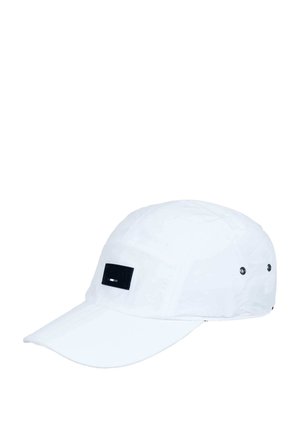 White cap with a rounded crown and short visor. Features a black rectangular tag on the front and ventilation eyelets on the sides.