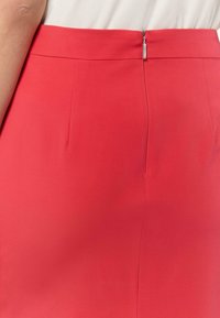 Rote Bleistiftrock mit glatter Textur, ausgestattet mit einem versteckten Reißverschluss auf der Rückseite und dezenten Nahtdetails.