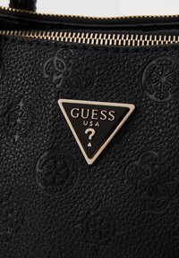 Sort tekstureret håndtaske med præget mønster, guldhardware og en trekantet logo med teksten "GUESS USA" og et spørgsmålstegn.