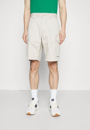Vaaleat beige cargo-shortsit, joissa on sivutaskut, valmistettu kevyestä kankaasta. Yhdistetty vihreään t-paitaan ja valkoisiin tennareihin, joissa on mustia yksityiskohtia.
