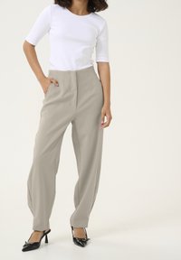 Lehké béžové kalhoty širokého střihu s vysokým pasem, s předními sklady. V kombinaci s upnutým bílým topem a černými lodičkami.