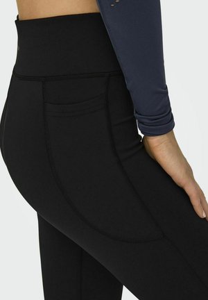 Leggings negros con una cintura alta, que cuentan con un bolsillo lateral y una textura suave. La costura es plana, creando un aspecto seamless.