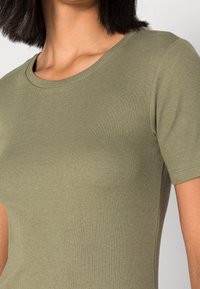 Maglietta a coste verde oliva con collo rotondo, maniche corte e texture sottile. Presenta un design aderente.