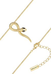 Zlatý prívesok v tvare hada s čiernymi očami na tenkom zlatom náhrdelníku, vybavený sponou v tvare homára a predlžovacím reťazcom s etiketou YOKOAMii.