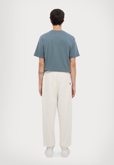 Light blue short-sleeve shirt paired with cream-colored, loose-fitting trousers. Trousers have a back pocket with elastic cuffs.