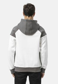 Sweatshirt mit Kapuze, weißem Körper und grauen Akzenten an Schultern und Kapuze. Verfügt über einen gerippten Saum und Bündchen, gefertigt aus weichem Material.