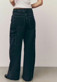 Weite Cargo-Jeans aus dunklem Denim mit großen Seitentaschen und fransigen Säumen. Auffällige Gesäßtaschen mit verstärktem Nähdetail.