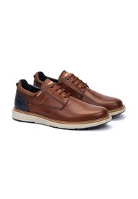 Scarpe in pelle marrone con finitura liscia, tacco nero a contrasto, punta rotonda e design con lacci. Suola in gomma con dettagli testurizzati.