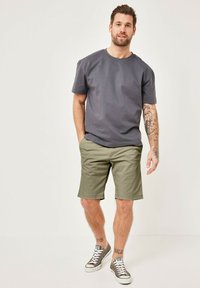 Graues Baumwoll-T-Shirt mit Rundhalsausschnitt, kombiniert mit olivgrünen Shorts. Graue Sneaker mit weißen Sohlen und schwarzen Schnürsenkeln.