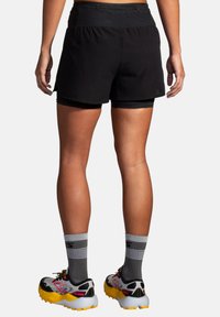 Shorts de sport noirs avec une taille élastique et une doublure intérieure. Portés avec des chaussures de course colorées et des chaussettes rayées grises. Ajustement réglable.