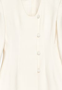 Neropuku, jossa on pyöreä kaula-aukko, jossa on viisi yhteensopivaa nappia edessä, rakenteelliset saumat ja sileä kangasaines.