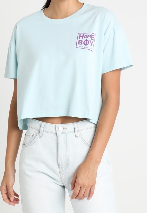 Světle modré zkrácené tričko vyrobené z bavlny, s čtvercovým purpurovým logem a textem "HOME BOY" na levé straně hrudi.