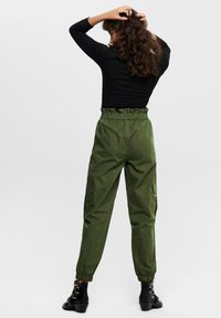 Grüne Cargo-Hosen mit elastischem Bund, Seitentaschen und Bündchen an den Knöcheln, kombiniert mit schwarzen offenen Sandalen mit Absatz und einem Langarmoberteil.