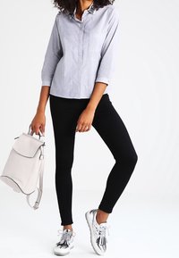 Jasnoniebieska koszula w paski na guziki z kieszenią, czarne legginsy i srebrne sneakersy. Jasnoszary plecak noszony na jednym ramieniu.