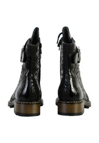 Botas de cuero negras hasta el tobillo con un acabado brillante, que presentan patrones en relieve, un cierre lateral y un tacón de madera. Detalle de hebilla cerca del tobillo.