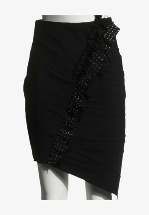 Jupe asymétrique noire avec un volant diagonal et un détail de bordure cloutée, sur un mannequin de la taille jusqu'à la moitié de la cuisse.
