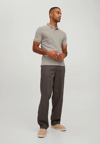 Polo gris clair avec col et bordure des manches contrastants, associé à un pantalon foncé et des chaussures beige à enfiler. Coupe légèrement ajustée.