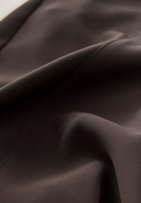 Tela de color marrón oscuro, textura suave, ligeramente reflectante, con un brillo sutil. Presenta un suave drapeado y costuras finas a lo largo de los bordes.