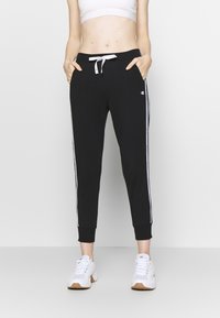 Černé joggingové kalhoty s bílými pruhy na bocích, s elastickým páskem na šňůrku, s manžetami na kotnících a kapsami. Vyrobené z měkké směsi bavlny.