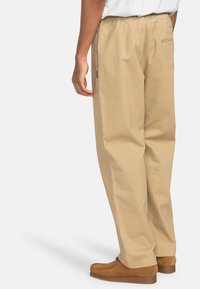 Khaki bomuldsbukser med løs pasform og elastisk talje. Har to sidelommer og en baglomme. Båret med brune slip-on sko.