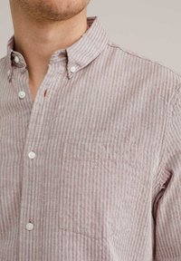 Camisa de botones a rayas en una tela suave y ligera; rayas en rosa claro y blanco; un bolsillo en el pecho; y un diseño de cuello clásico.