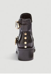 Bottine en cuir noir avec un bout rond, quincaillerie dorée, boucle sur le côté et clous décoratifs dorés le long du dos. Talon épais pour un bon soutien.