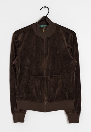 Veste zippée en velours brun foncé avec col, poignets et ourlet côtelés, poches avant, suspendue sur un cintre noir sur fond blanc.