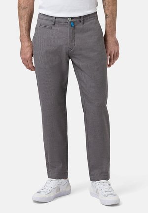 Grau gemusterte Hose mit geradem Schnitt, versehen mit einem Reißverschluss und Knopfverschluss. Akzentuiert mit einem blauen Etikett. Getragen mit weißen Sneakers.