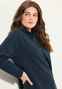 Mörkblå zip-up huvtröja med långa ärmar, mjuk textur, hög krage och sidofickor. Har en halvdragkedja för enkel påklädning.