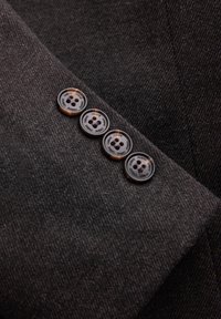 Tejido gris texturizado con cuatro botones marrones con detalles en negro, fijados en el puño de una prenda.