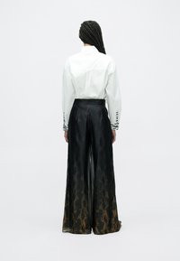 Wit overhemd met zwart gestreepte manchetten gecombineerd met wijd uitlopende, hooggesloten zwarte broek met een subtiel gouden patroon en een gladde textuur.