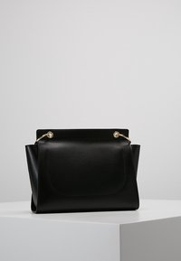 Czarna torebka w strukturze, wykonana z teksturowanego materiału, z zaokrąglonymi krawędziami i złotymi akcentami. Posiada przednią kieszeń oraz charakterystyczną klapkę na górze.