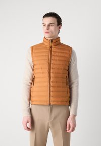 Narančasti prešani puffer prsluk s visokim ovratnikom, prednjim zatvaračem, bočnim džepovima i detaljem loga s lijeve strane. Teksturirani završetak tkanine.