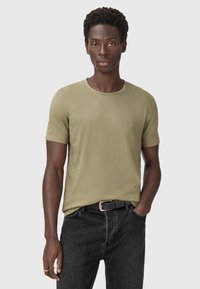T-shirt a maniche corte verde oliva realizzato in tessuto morbido, con scollatura rotonda e un logo discreto sul lato sinistro del petto. Abbinato a jeans neri.