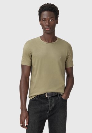 T-shirt à manches courtes olive en tissu doux, avec un col rond et un logo subtil sur la poitrine gauche. Associé à un jean noir.