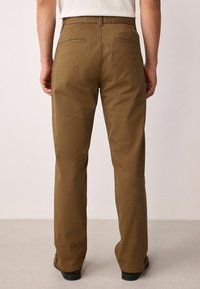 Bruine katoenen broeken met een rechte pasvorm, voorzien van twee achterzakken en een eenvoudig ontwerp van de tailleband. Katoenen textuur en op maat gemaakte snit.