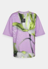 Lila t-shirt med en blommig design som har gröna och vita inslag, rundad hals, korta ärmar och en fyrkantig logotypapplikation.