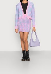 Pletený růžovo-modrý kostkovaný kardigan s cropped designem a knoflíky, doplněný o odpovídající mini sukni a lila kabelku. Černé bojové boty.