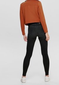 Czarne skinny jeans w połączeniu z czerwonobrązową, krótką kurtką. Materiał jest gładki, z dopasowanym fasonem i minimalną ilością elementów metalowych.