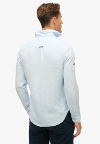 Lichtblauw, lange mouwen overhemd met kraag en achterste vent, voorzien van een textuurstof en contrasterende stikseldetails.