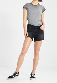 Harmaa istuva t-paita käännetyillä hihoilla, mustat farkku shortsit repaleisella helmalla ja mustat lenkkarit valkoisilla pohjilla. Yksinkertainen rento tyyli.