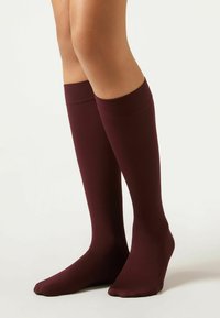Knielange burgunderfarbene Socken aus einem glatten, dehnbaren Material mit einem gerippten oberen Bund und einem nahtlosen Zehenbereich.