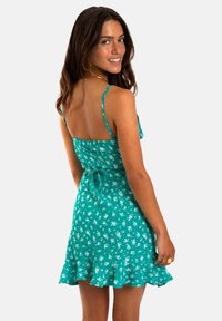 Teal bloemen-zomerjurk met dunne bandjes, aansluitende bovenkant en uitlopende gerUFFelde zoom. Heeft een gestrikt achterpand voor een verstelbare pasvorm.