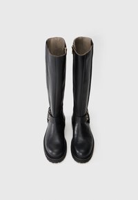 Par de botas de cuero negro hasta la rodilla con cremalleras laterales y correas con hebillas sobre suelas gruesas en un fondo blanco.
