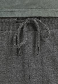 Graue Sweatpants aus strukturiertem Stoff, mit einem gerippten Bund, Kordelzug und schwarzen Plastikkappen am Kordelzug.